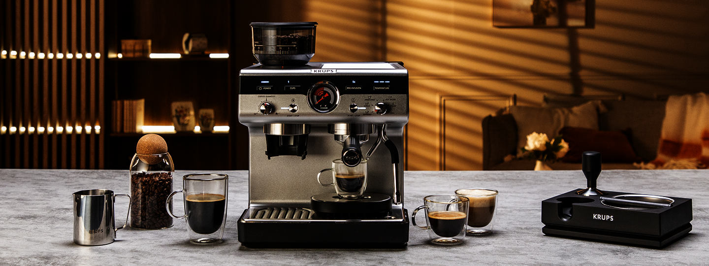 Krups Kaffeeautomat mit Zubehör im Hintergrund, wie Kaffebohnen, Kaffetassen