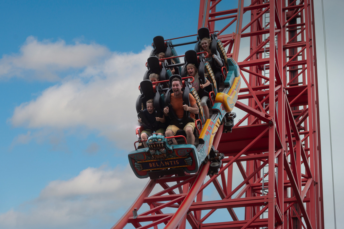 Menschen in einem Achterbahnwagen schreien vor Freude und Nervenkitzel während einer steilen Abfahrt auf der rotgestützten Bahn „Huracan“ im Freizeitpark Belantis.