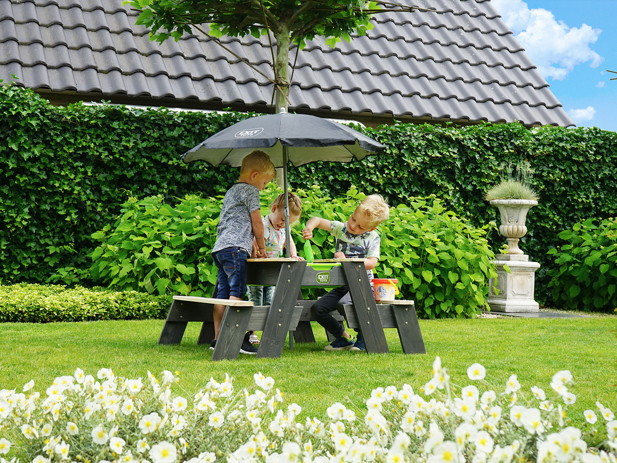 Drei Kinder spielen im Garten mit eimer und Schaufel an einem kleinen Tisch mit Schrim