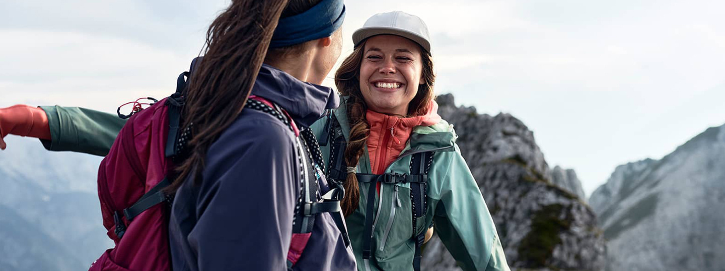 Zwei junge Frauen in Funktionskleidung die sich in den Bergen umarmen