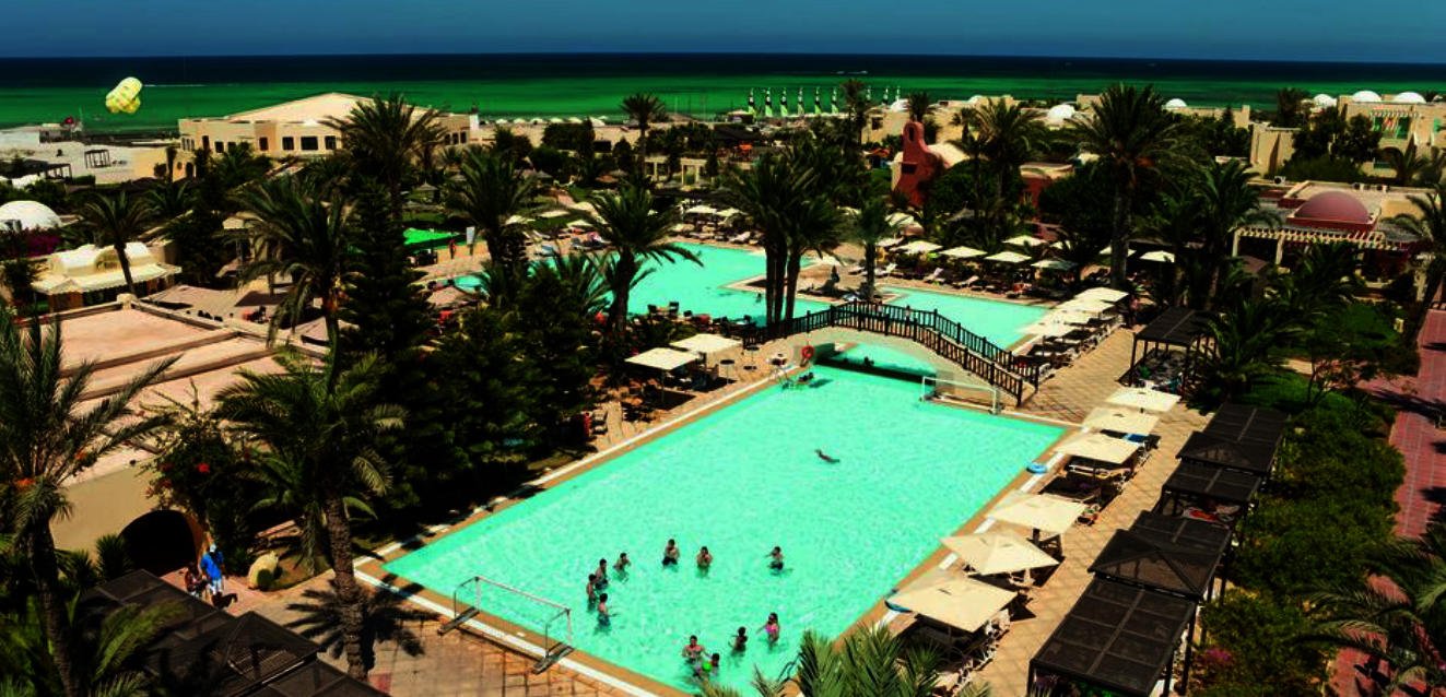 Hotel aus Vogelperspektive mit zwei Pools, Meer im Hintergrund & vielen Palmen